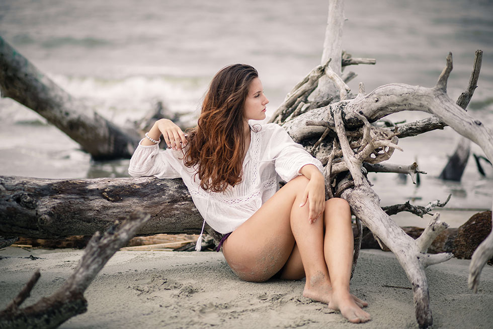 Photo of a woman sitting on the beach against a piece of driftwood