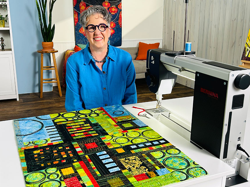 Susan Brubaker Knapp on the set of Quilting Arts TV, with a quilting machine and one of her art quilts